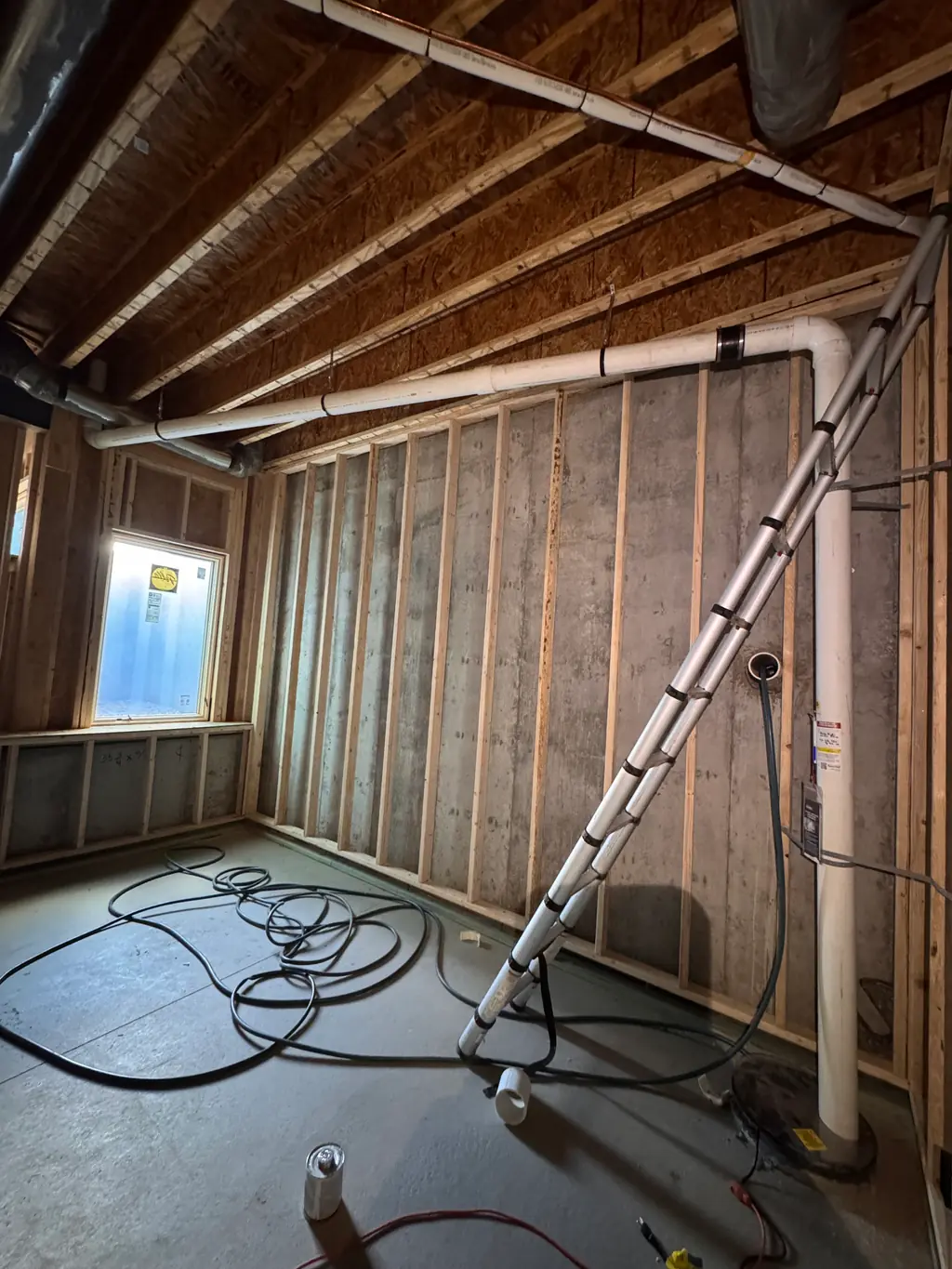 Radon pipe running up an unfinished basement wall and along the floor joists