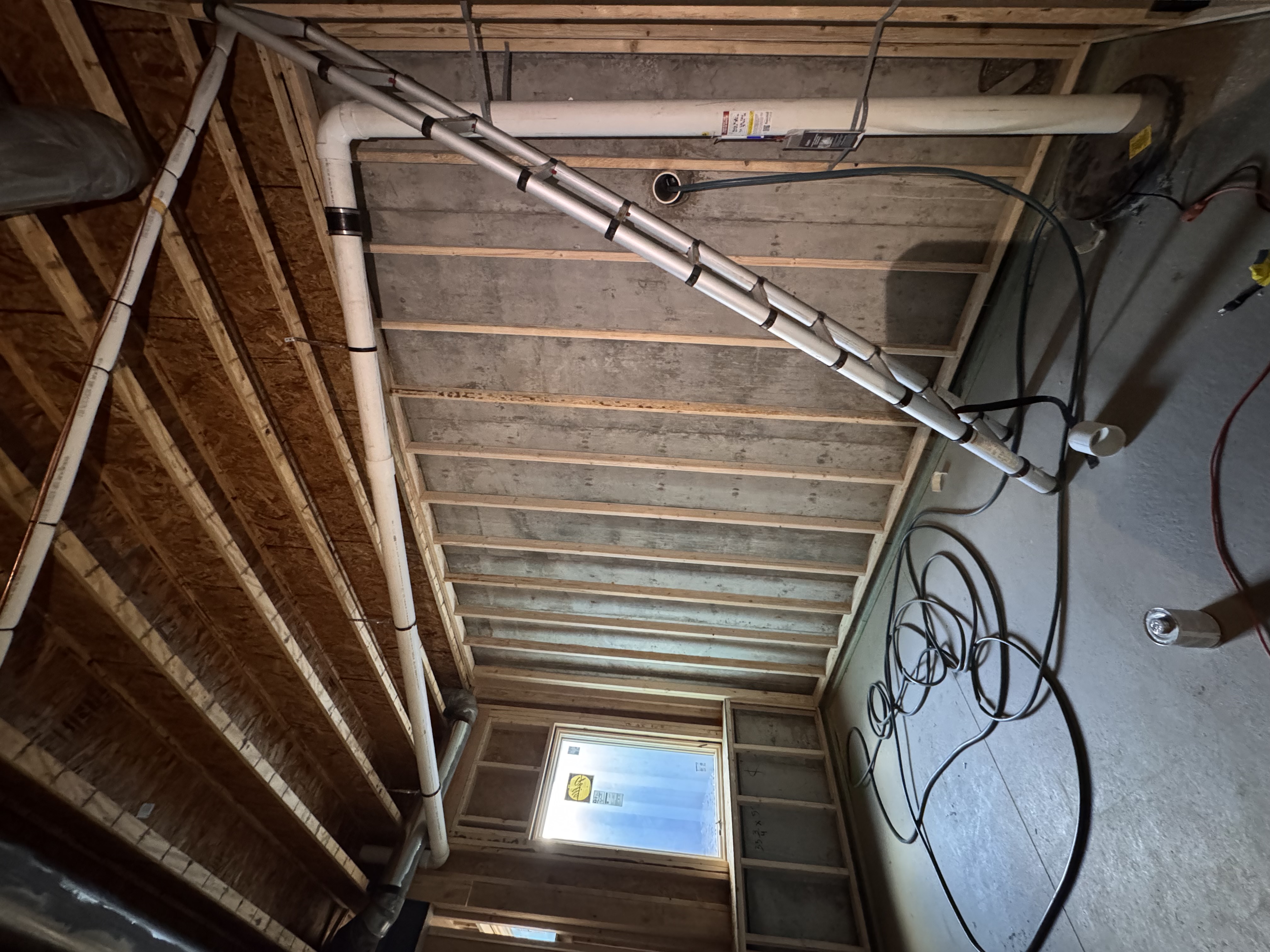 Radon pipe running up an unfinished basement wall and along the floor joists